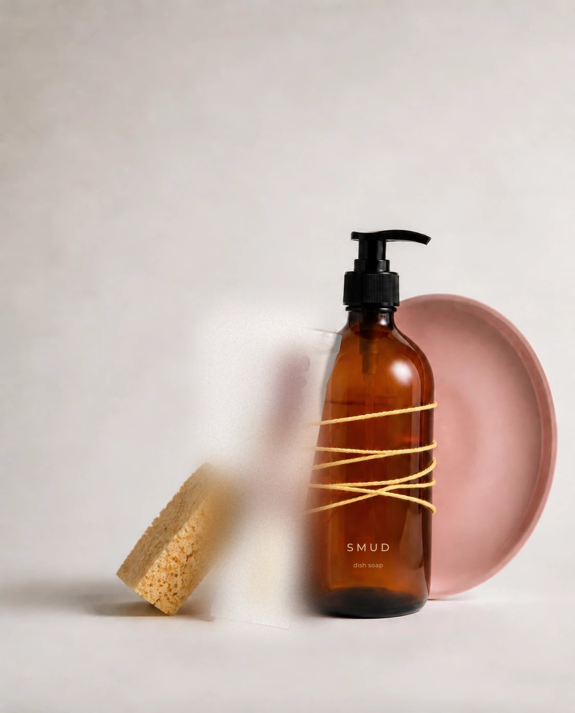 SMUD dish soap bottle and powder stick tied together with butter-yellow string, with a sponge and a pink plate